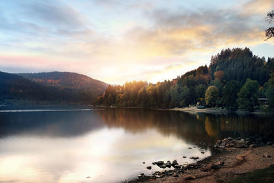 Scenic view of lake by trees against sky at sunset