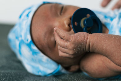 Tranquil adorable sleepy newborn baby lying wrapped on blue cozy blanket using pacifier