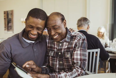 Cheerful senior man sharing smart phone with male nurse at retirement home