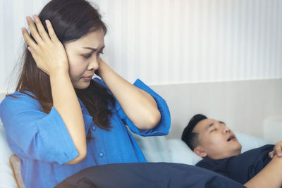 Close-up of woman covering ears while sitting by man snoring