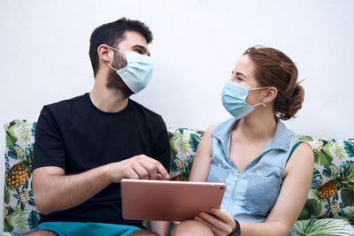 A couple with surgical masks are while using a tablet