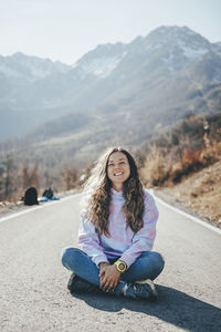 Carefree woman sitting cross-legged on road in front of mountains
