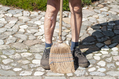 Gardener in dirty work clothes and boots holds garden tools, tools brush broom