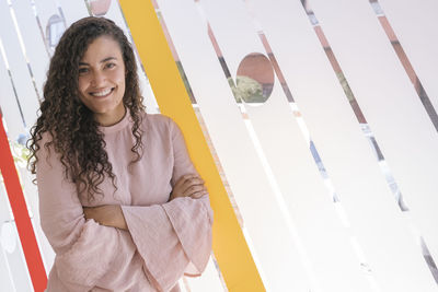 Portrait of smiling young woman with arms crossed standing in office