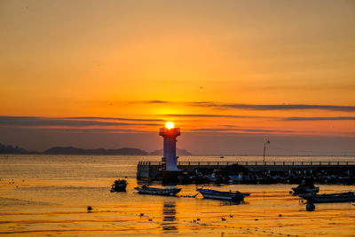 Lighthouse by sea against sky during sunset