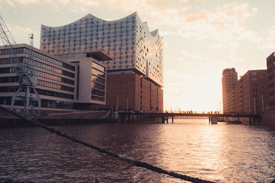 River by buildings against sky during sunset