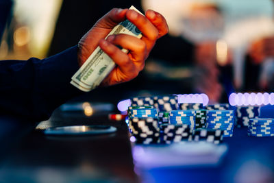 Male gambler sitting near roulette with cash dollars in his hands and there is casino chips 