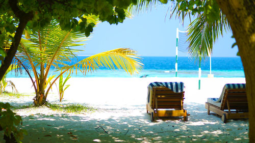 Deck chairs on beach against sky