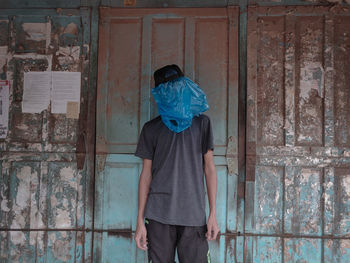 Man wearing plastic on face while standing against closed old door