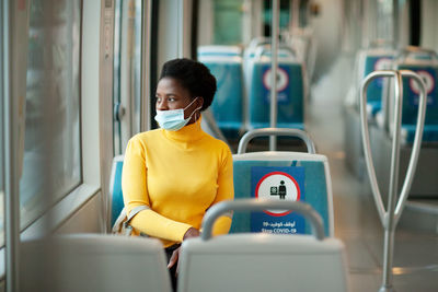 African woman wearing a protective mask rides on a bus and looks out the window, social distance.