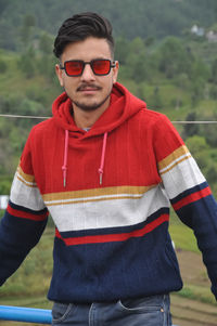 A handsome indian young guy wearing sunglasses, standing outdoor with looking at camera 