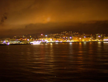 Illuminated city by sea against sky at night