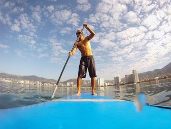 Full length of shirtless man paddleboarding in sea