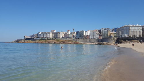 View of calm sea in front of buildings against clear sky