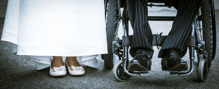 Low section of bride standing by bridegroom on wheelchair