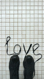 Directly above shot of text made with shoelaces and black canvas shoes on white tiled floor