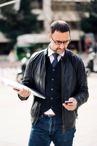 Middle aged ethnic male entrepreneur text messaging on cellphone while standing in city