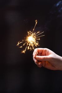 Cropped hand holding sparkler at night