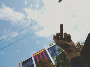 Low angle view of cropped hand holding camera against sky