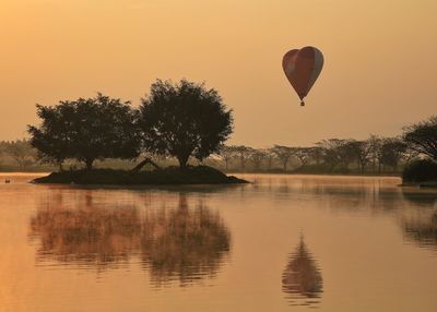 Hot air balloon flying over lake against sky during sunset