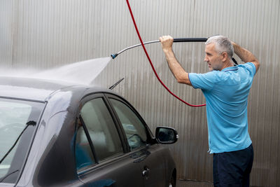Man cleans automobile with covered with foam shampoo chemical detergent during carwash self service