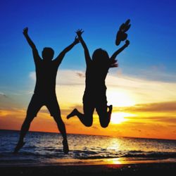 Silhouette people jumping on beach against sky during sunset