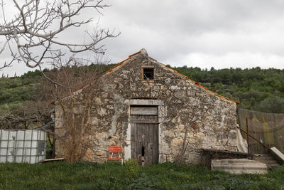 Old building by trees on field against sky