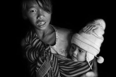 Portrait of boy carrying sister against black background