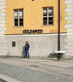 Full length of man standing on footpath against building