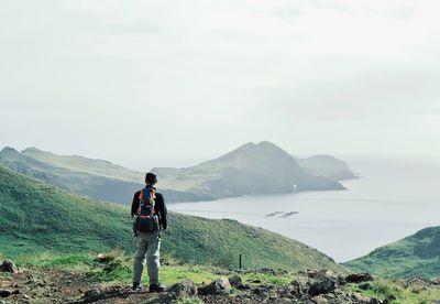 Rear view of man standing on mountain against sky