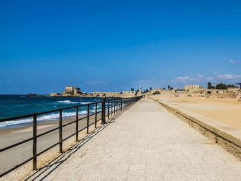 Pathway with railing at beach against blue sky