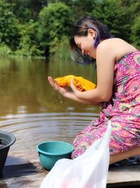 Side view of young woman holding while standing by lake