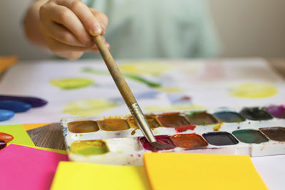 Cropped hand of boy holding paintbrush over palette while painting at classroom