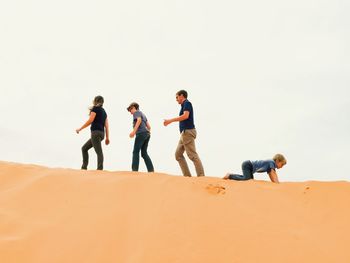 Low angle view of family on sand dune at desert against clear sky