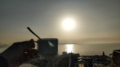 Person holding ice cream by sea against sky during sunset