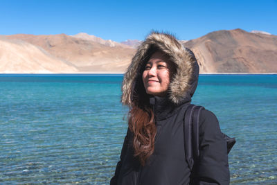 Smiling woman standing by lake against mountains