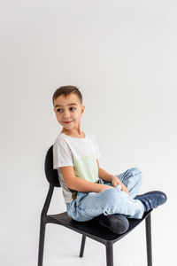 Portrait of boy sitting on chair against white background