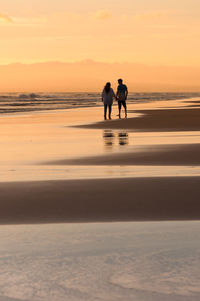 Silhouette people on beach against sky during sunset