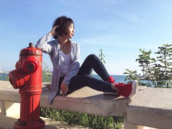 Full length of woman sitting on retaining wall against sky