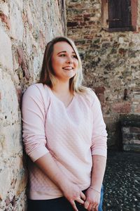Portrait of smiling young woman standing against brick wall