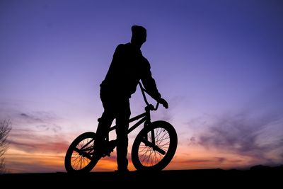 Silhouette man riding bicycle against sky during sunset