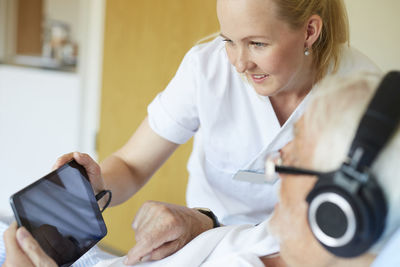 Smiling female nurse using digital tablet with senior man in hospital ward