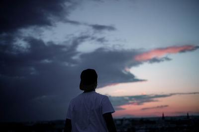 Rear view of man standing at beach against sky during sunset