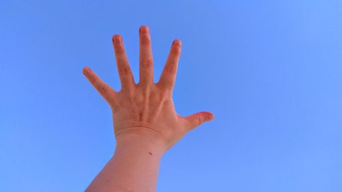 Cropped hand of woman reaching against clear blue sky