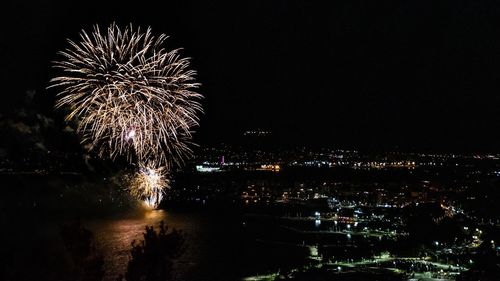 Firework display over illuminated city against sky at night