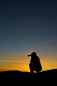 Silhouette man photographing on land against sky during sunset