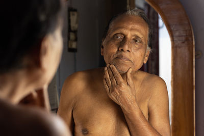 An old indian man in front of mirror checking himself