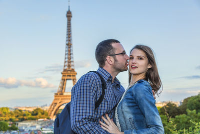 Man kissing girlfriend while standing against eiffel tower