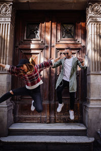 Full length of happy friends jumping on steps at doorway