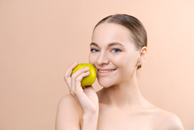 Portrait of young woman holding apple against yellow background